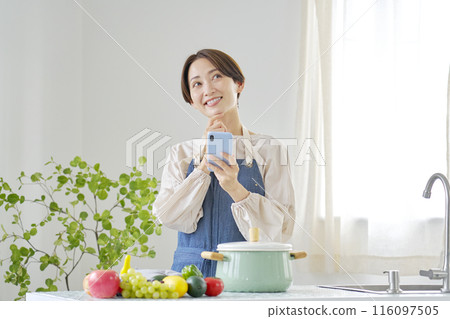 一位女士在廚房一邊使用智慧型手機一邊想像 116097505