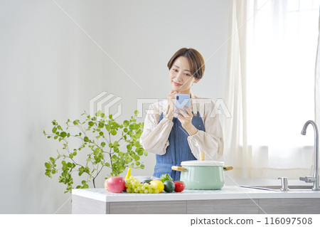 觀看一個智能手機的婦女在廚房裡 116097508