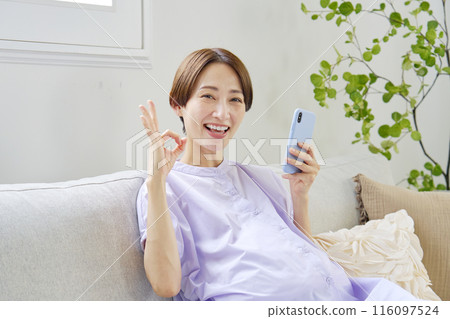A pregnant woman with a high-grade pregnancy making an OK sign with a smartphone at home A pregnant woman with a high-grade pregnancy making an OK sign with a smartphone at home 116097524