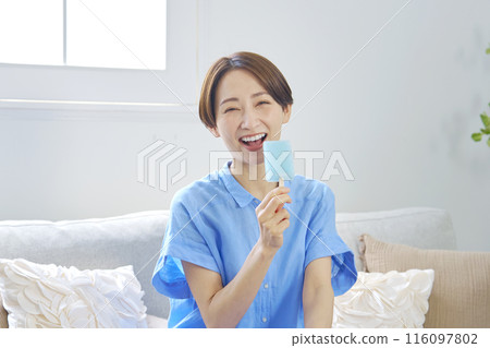 Woman eating popsicle at home looking at camera 116097802