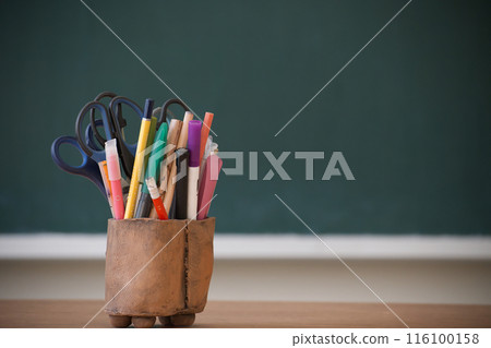 Classroom supplies in a wooden holder in front of a chalkboard 116100158