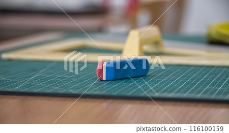 Close-up of a blue and red eraser on a green cutting mat in an art studio 116100159