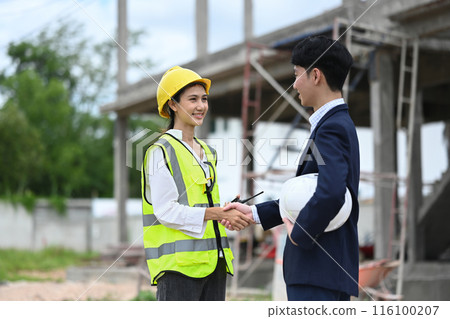 Handsome businessman in black suit and engineer shaking hands on construction site 116100207