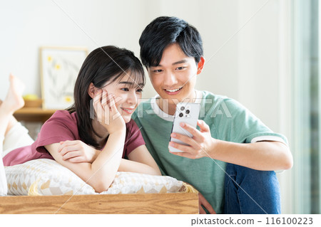 Young couple looking at a smartphone in the living room 116100223