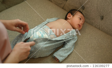 Above view of mother dressing newborn baby lying on couch. Childcare and motherhood concept 116100277