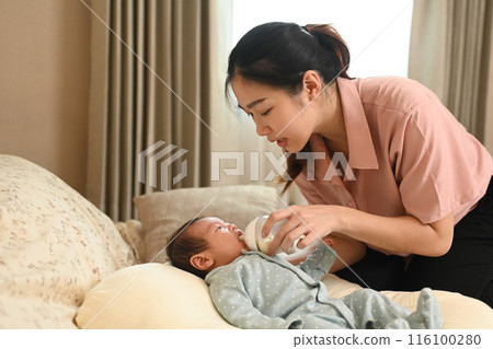 Caring mother feeding her baby with bottle and in living room on the sofa. Healthy infant nutrition concept Caring mother feeding her baby with bottle and in living room on the sofa. Healthy infant nutrition concept 116100280