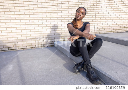 On city steps, a fashionable young lady in a trendy black outfit exudes confidence and style On city steps, a fashionable young lady in a trendy black outfit exudes confidence and style 116100859