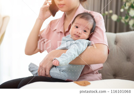 A busy Asian mom is talking on the phone while holding her newborn baby son on a couch at home. A busy Asian mom is talking on the phone while holding her newborn baby son on a couch at home. 116101068