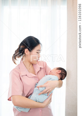 A happy Asian mom is talking and comforting her infant baby son while holding him in her arms. A happy Asian mom is talking and comforting her infant baby son while holding him in her arms. 116101098