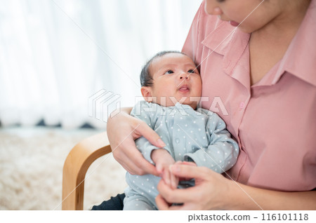 A cute baby son is in his mom's embrace on an armchair, looking at her while she talks to him. 116101118