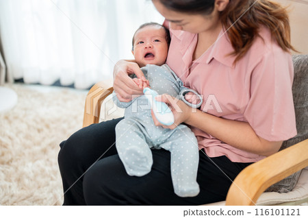 A caring Asian mom is trimming her newborn baby's nails on an armchair in the living room. 116101121