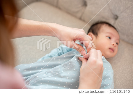 A caring mom is putting pajamas on her newborn baby son on a couch in the living room. 116101140