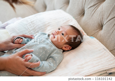 An adorable Asian newborn baby son in blue pajamas is in his bed, talking and playing with his mom. An adorable Asian newborn baby son in blue pajamas is in his bed, talking and playing with his mom. 116101142