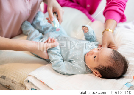 An infant baby boy is having his nails trimmed by an electronic baby nail trimmer held by his mom. 116101148
