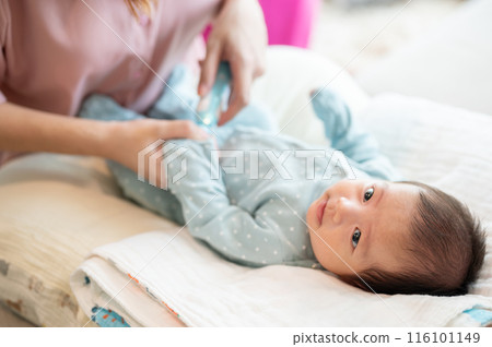 An infant baby boy is having his nails trimmed by an electronic baby nail trimmer held by his mom. 116101149