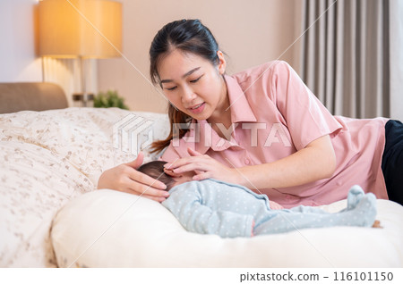 A beautiful young Asian mom is comforting and putting her newborn baby son to sleep in the bedroom. 116101150