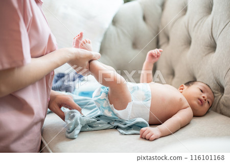 A caring mom is changing her newborn baby's clothes and diaper on the couch in the living room. 116101168