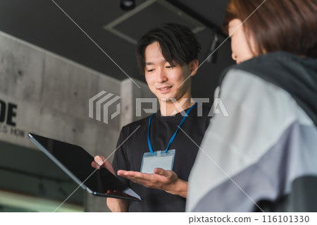 A young Asian male trainer/instructor explaining and instructing a female member on an exercise menu at a gym A young Asian male trainer/instructor explaining and instructing a female member on an exercise menu at a gym 116101330