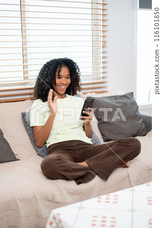A young, cheerful Black woman is talking on a video call via her smartphone with her friends at home 116101850
