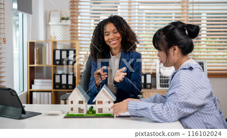 A Black female real estate agent is having a meeting with her client, showing the house model. 116102024