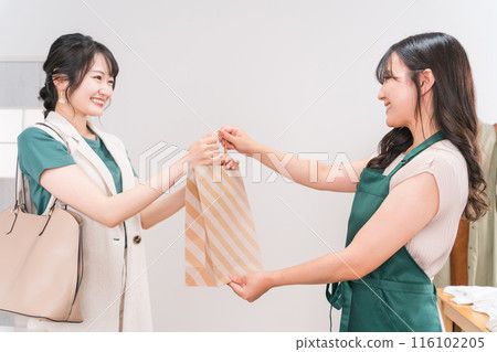 A young Asian woman shopping at an apparel store and receiving products from a shop assistant and a female shop assistant A young Asian woman shopping at an apparel store and receiving products from a shop assistant and a female shop assistant 116102205