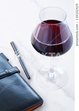 Image of a person sipping red wine and writing in a black leather organizer Image of a person sipping red wine and writing in a black leather organizer 116102420