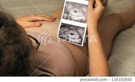 Expectant Parent with Ultrasound Scan. A pregnant person is seen holding an ultrasound scan over their belly, symbolizing anticipation and connection with the unborn child. Expectant Parent with Ultrasound Scan. A pregnant person is seen holding an ultrasound scan over their belly, symbolizing anticipation and connection with the unborn child. 116102688