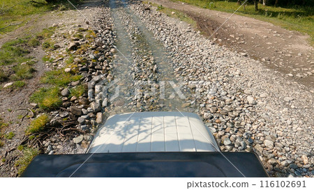 Off-road adventure across a creek. First-person view from a vehicle crossing a shallow rocky creek in a mountainous area on a bright day. Off-road adventure across a creek. First-person view from a vehicle crossing a shallow rocky creek in a mountainous area on a bright day. 116102691