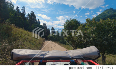 Off-road Adventure in Forested Terrain. A first-person view from a vehicle driving on a dirt road, surrounded by lush greenery under a clear blue sky. Off-road Adventure in Forested Terrain. A first-person view from a vehicle driving on a dirt road, surrounded by lush greenery under a clear blue sky. 116102694