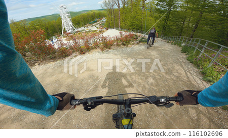 First-person view of a cyclist riding on a gravel path in a forest. Another cyclist can be seen ahead on the path. A cycling adventure on a mountain bike. First-person view of a cyclist riding on a gravel path in a forest. Another cyclist can be seen ahead on the path. A cycling adventure on a mountain bike. 116102696