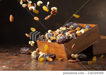 Dates, nuts, and raisins in a wooden box on a brown background. Dates, nuts, and raisins in a wooden box on a brown background. 116104380