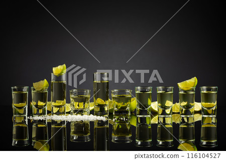 Tequila shots with lime slices and salt on a black reflective background. Tequila shots with lime slices and salt on a black reflective background. 116104527