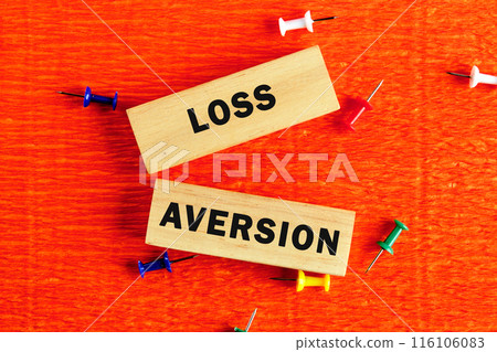 LOSS AVERSION text written on wooden blocks with a hand on an orange background LOSS AVERSION text written on wooden blocks with a hand on an orange background 116106083