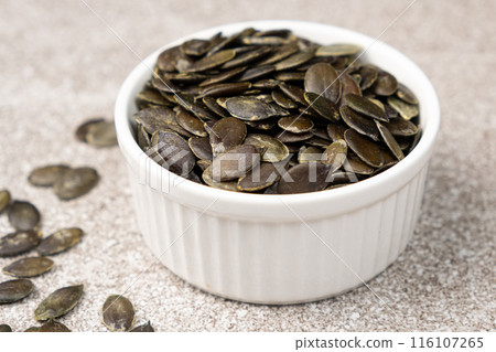Peeled pumpkin seeds in plate on gray stone background, close-up Peeled pumpkin seeds in plate on gray stone background, close-up 116107265