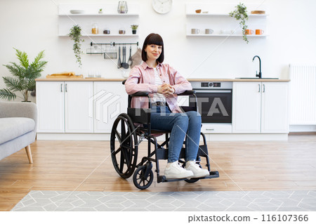 Woman in wheelchair sitting in modern kitchen interior Woman in wheelchair sitting in modern kitchen interior 116107366
