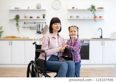 Happy mother in wheelchair with daughter in kitchen 116107406