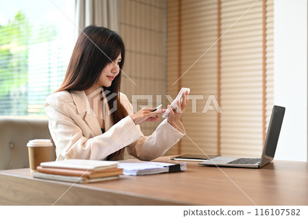 Portrait of Asian female accountant making calculations checking marketing report at office desk Portrait of Asian female accountant making calculations checking marketing report at office desk 116107582