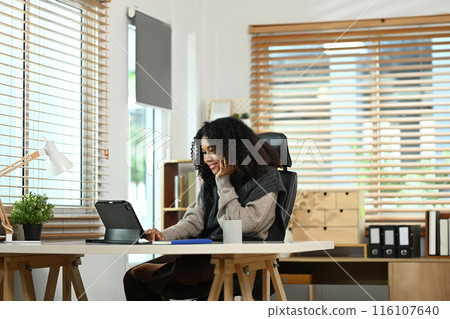 Cheerful young woman with curly hair using digital tablet remote working at home online Cheerful young woman with curly hair using digital tablet remote working at home online 116107640