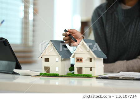 Realtor hand pointing to the house model and explaining contract to client. New house and real estate concept 116107734