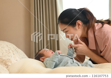 Happy young asian mother touching her newborn baby lying on sofa at home. Childcare and motherhood concept 116107753