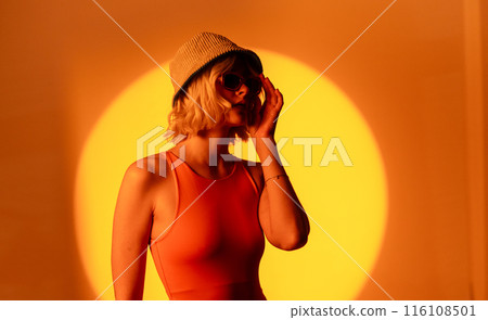 Stylish female model with light natural makeup wearing trendy sunglasses against orange background 116108501
