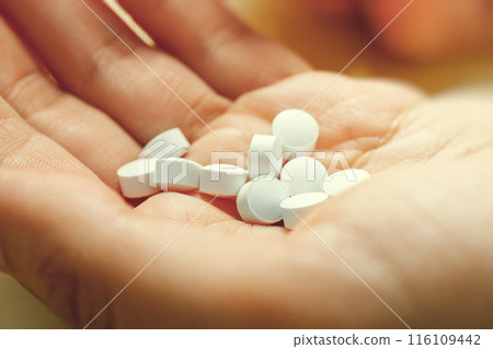 White round medical pills lie in hand, close up. These could be vitamins or antibiotics or pain relievers or any other. White round medical pills lie in hand, close up. These could be vitamins or antibiotics or pain relievers or any other. 116109442