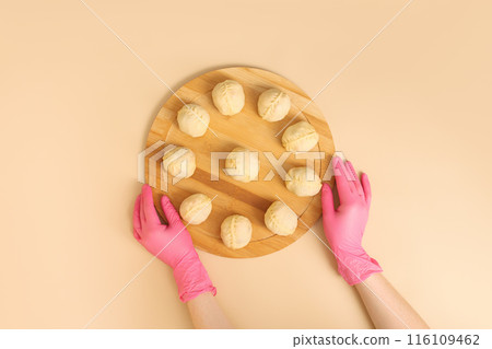 Top view of hands wearing rubber gloves arranging traditional Central Asian manti with meat on a wooden board, frozen semi-finished products. 116109462