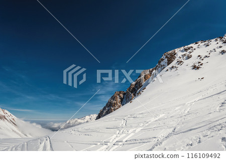 Majestic Winter Landscape: Stunning Views of Central Asian Mountains Above the Clouds with Ski and Snowboard Tracks in Kazakhstan's Almaty Region. 116109492