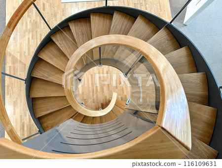 A spiral staircase made of wood and glass. The staircase is curved and has a glass railing 116109631