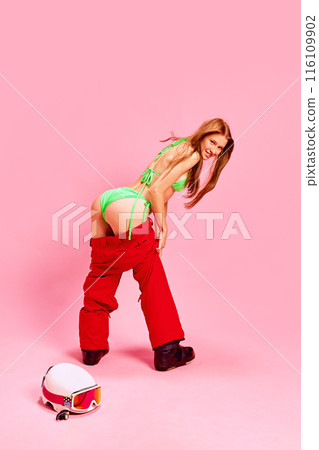 Woman combining summer and winter attire, showcasing her fit body with funny pose against pink studio background. Summer vs winter 116109902