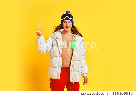 Energetic young woman in vibrant winter gear, expressing happiness and enthusiasm, against bright yellow studio background. Ready for vacation Energetic young woman in vibrant winter gear, expressing happiness and enthusiasm, against bright yellow studio background. Ready for vacation 116109916
