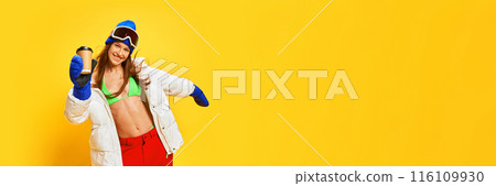 Coffee break. Smiling and happy young girl with slim tanned body, in bikini and winter clothes posing against bright yellow studio background 116109930