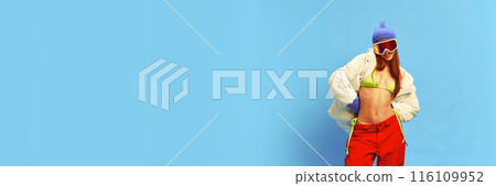 Athletic woman in a mix of summer and winter gear posing against blue studio background. rom summer into winter Athletic woman in a mix of summer and winter gear posing against blue studio background. rom summer into winter 116109952