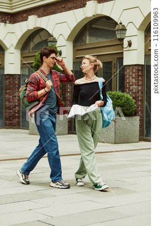 Young stylish guy and girl, university students, friends walking outdoors the campus and lively talking, discussing personal and school life 116109963